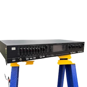 Può includere: Un equalizzatore di frequenza stereo nero ADC Sound Shaper modello SS-200SL dotato di molteplici cursori verticali per la regolazione della frequenza sinistra e destra, un display analizzatore di spettro centrale, un tasto di accensione e un jack microfono.