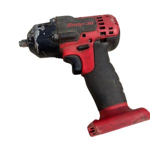 Puede incluir: Una llave de impacto inalámbrica roja y negra con el logotipo de Snap-on en el lateral. La herramienta tiene una carcasa frontal de metal negro con desgaste visible, un mango de goma negro, un gatillo rojo y una base roja para la batería.