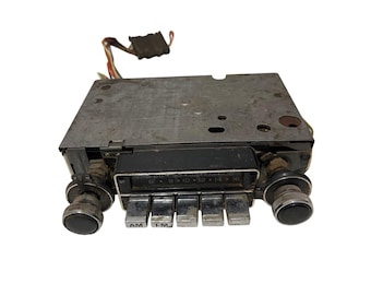 Può includere: Autoradio vintage con frontalino in metallo e manopole cromate. La radio ha pulsanti AM e FM, un quadrante di sintonizzazione e una serie di pulsanti. I fili si estendono dalla parte superiore. Progettato per adattarsi al cruscotto di un'auto.