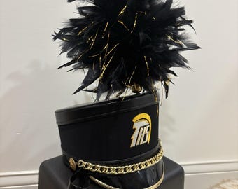 May include: Black and gold marching band hat with a black feather plume and a gold chain. The hat has the letters "THS" embroidered on the front.