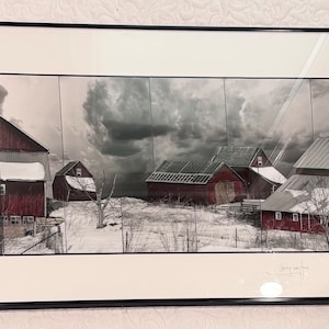 May include: A framed black and white photograph of red barns in a snowy landscape. The sky is cloudy and dramatic. The barns are in various states of repair, with some having snow on their roofs. The photograph is titled "Days of the Past" and signed by the artist.