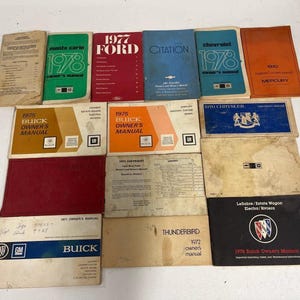 May include: A collection of vintage automotive owner's manuals from the 1970s, featuring various brands including Buick, Ford, Chevrolet, and Mercury. The manuals are rectangular, printed in diverse colors like red, blue, orange, and black, with text.