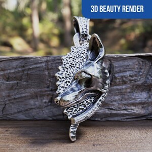Puede incluir: Colgante de plata con un diseño detallado de cabeza de lobo sobre un fondo texturizado. El colgante tiene un bucle en la parte superior para sujetar una cadena.