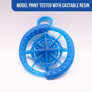 Peut inclure: Pendentif bleu clair imprim&eacute; en 3D avec une rose des vents dans un cadre circulaire. Le cadre pr&eacute;sente un motif textur&eacute; en forme de tentacules. Le texte "MODEL PRINT TESTED WITH CASTABLE RESIN" est en haut. Le pendentif a une boucle pour accrocher.