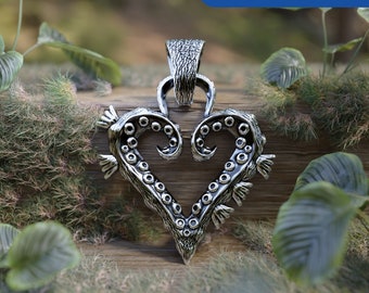 Peut inclure: Un pendentif en argent en forme de cœur avec des détails complexes ressemblant à une pieuvre. Le pendentif est sur une surface en bois avec de la végétation verte en arrière-plan.