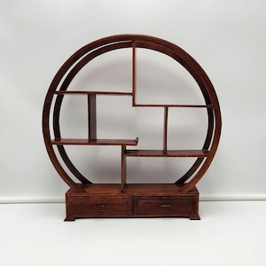 May include: A dark brown, wooden, circular shelf unit with multiple shelves and two drawers at the base. The design features a large circular frame with rectangular shelves and supports, creating a unique display space.
