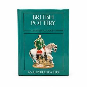 May include: A hardback book titled British Pottery: An Illustrated Guide by Geoffrey A. Godden. The cover is dark teal with a central image of a ceramic figurine depicting a person in a green tunic riding a white horse on a tan base.