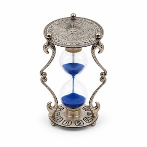 May include: An hourglass with a metallic antique silver finish frame featuring ornate curved supports. The top and bottom plates are engraved with celestial sun motifs and Roman numerals. The central glass bulb contains vibrant blue sand.