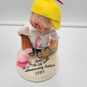 May include: A collectible doll wearing a yellow propeller cap, white shirt with pink accents, and holding an ice cream cone. The doll stands on a circular base printed with Annalee Doll Society 10th Anniversary Edition 1993. A pink pom-pom sits on the base.