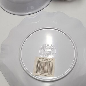May include: A white plastic shell-shaped plate, a white bowl labeled 5-1/2 inch bowl with rim, and a plastic-wrapped tumbler featuring Little Mermaid graphics. Each item has a barcode sticker and manufacturer markings on the underside.