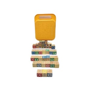 May include: A set of wooden alphabet blocks with a yellow carrying case. The blocks are arranged in a pyramid shape and feature letters, numbers, and symbols. The case has a handle for easy transport.