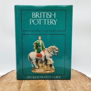 May include: A teal book titled "British Pottery" by Geoffrey A. Godden. The cover features a ceramic figurine of a person on horseback. The book is an illustrated guide.