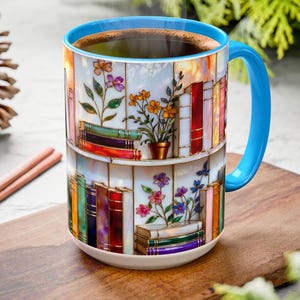 May include: A ceramic coffee mug with a blue handle and rim, filled with dark liquid. The mug features a colourful design of bookshelves with flowers. The mug sits on a wooden chopping board, with a pine cone and cinnamon sticks nearby.