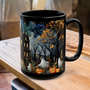 May include: Black ceramic mug with a Halloween-themed design. The design features a haunted house, ghosts, pumpkins, and a starry night sky. The mug has a large handle and is sitting on a wooden surface.