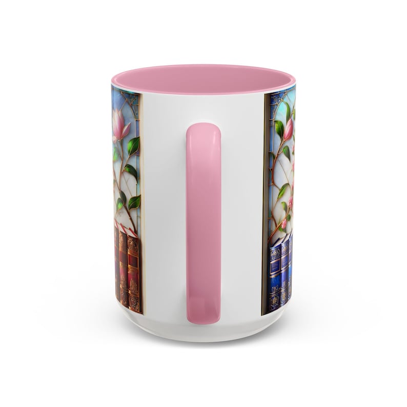 May include: White ceramic mug with a pink interior and handle. The mug features a stained-glass design with pink flowers and books. The handle is a solid pink color. The mug is a standard size for coffee or tea.
