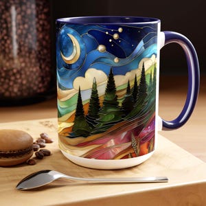 May include: A large ceramic mug with a colorful stained-glass design featuring a crescent moon, stars, and a forest scene. The mug has a white base, a dark blue interior, and a matching handle. The design includes shades of blue, green, gold, and red.