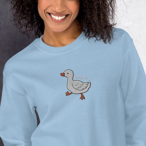 May include: Light blue sweatshirt with an embroidered image of a gray duck with the text "Silly Duck" above it.