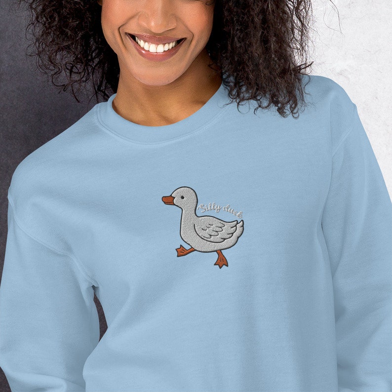 May include: Light blue sweatshirt with an embroidered image of a gray duck with the text "Silly Duck" above it.