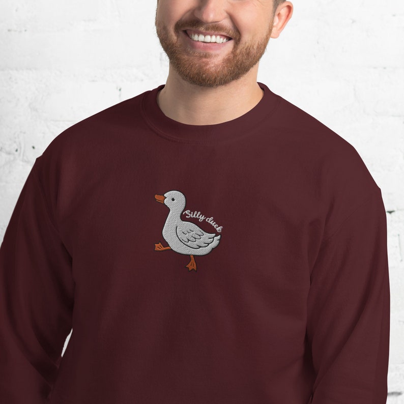 May include: A maroon sweatshirt with a white embroidered duck and the text "Silly duck" in brown.