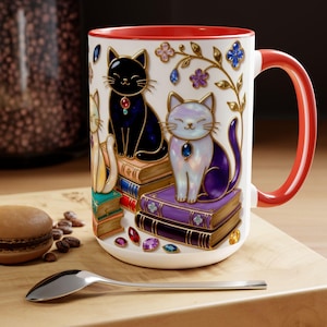 May include: White ceramic mug with a red interior and handle, featuring three cat illustrations sitting on books. The cats are black, white, and yellow, adorned with jewels. Floral and jewel accents decorate the mug's exterior.
