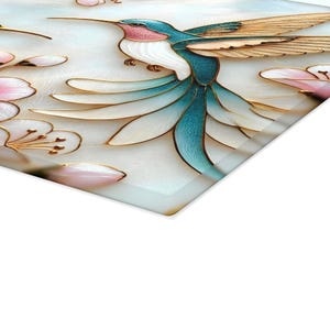 Pode incluir: Pe&ccedil;a de arte decorativa com um beija-flor com plumagem azul, branca e rosa, acentuada com detalhes dourados. O design inclui flores estilizadas em rosa e branco. A obra de arte est&aacute; em um fundo claro.