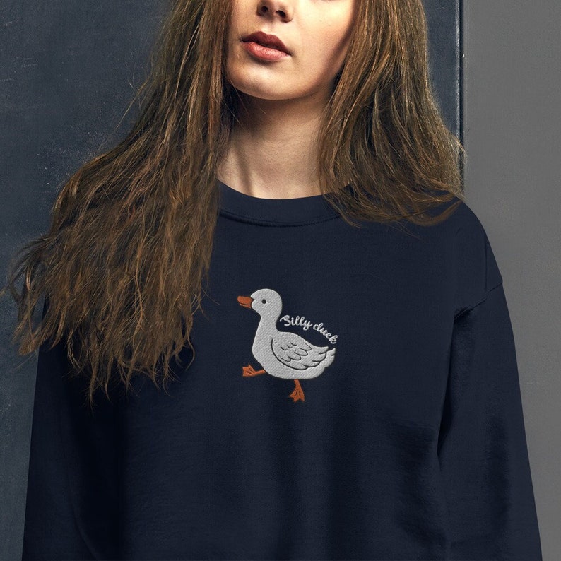 May include: A navy blue sweatshirt with a white embroidered cartoon duck and the text "Silly duck" in orange.