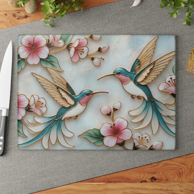Pode incluir: T&aacute;bua de corte retangular com dois beija-flores com plumagem turquesa e rosa e asas douradas. As aves s&atilde;o cercadas por flores de cerejeira rosa e folhas verdes sobre um fundo azul claro.