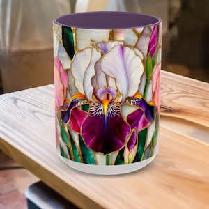 May include: A cylindrical mug featuring a stained-glass style iris design. The floral pattern includes white, purple, pink, and yellow hues, outlined with gold. The interior is a solid purple, and the base is white.