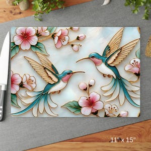 Pode incluir: T&aacute;bua de corte retangular com um design de beija-flor e floral. A t&aacute;bua apresenta dois beija-flores com detalhes em verde-azulado, rosa e dourado, rodeados por flores rosa e folhas verdes. A t&aacute;bua mede 28 cm x 38 cm.