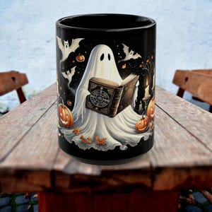 Pode incluir: Caneca de cerâmica preta com um design temático de Halloween. O design inclui um fantasma branco lendo um livro, abóboras, morcegos e um céu estrelado. A caneca é decorada com folhas de outono e velas.