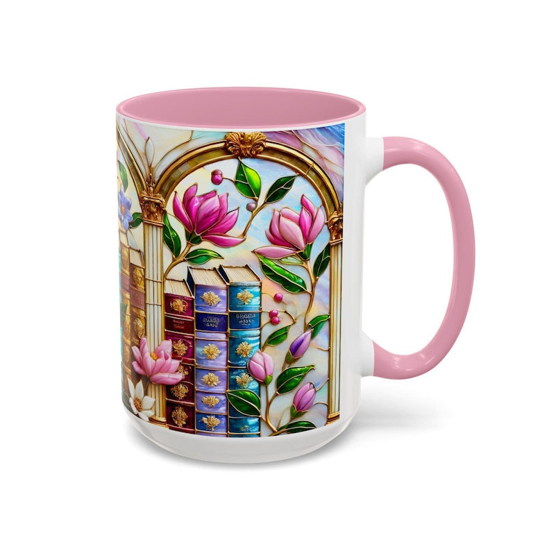 May include: White ceramic mug with a pink interior and handle. The mug features a stained-glass design with pink flowers, green leaves, and stacks of books. Gold trim outlines the design.