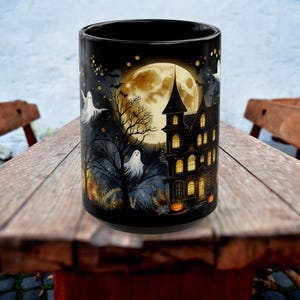 May include: Black ceramic Halloween mug featuring a spooky haunted house, ghosts, and a full moon. The design includes bats, trees, and pumpkins, creating a festive and eerie atmosphere. Perfect for enjoying your favorite beverage during the Halloween season.