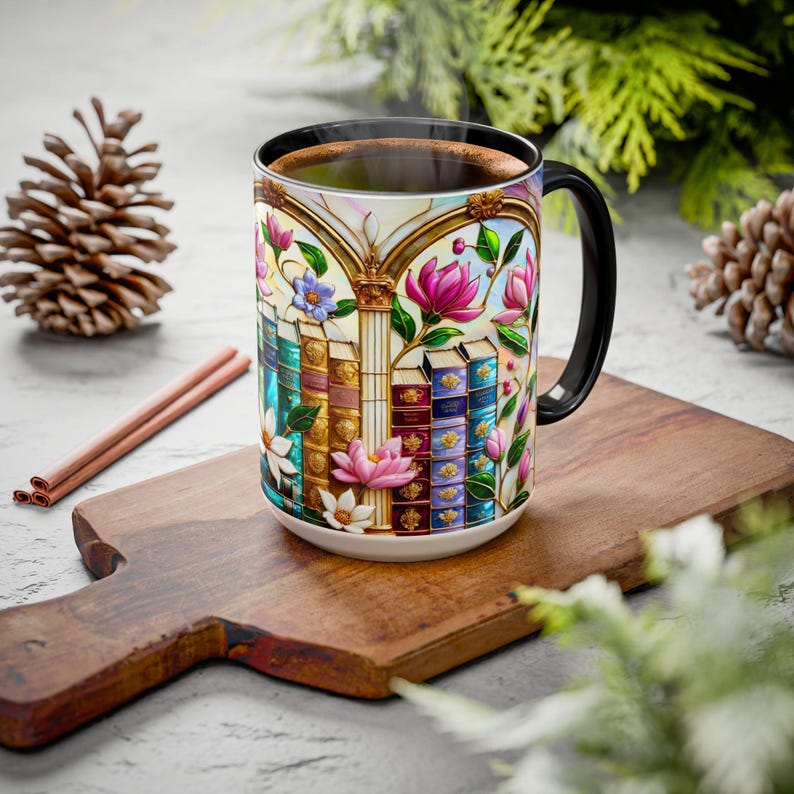 May include: A ceramic coffee mug with a black handle and rim, featuring a colorful stained-glass design of books, flowers, and architectural elements. The mug is filled with a dark liquid, likely coffee or tea.