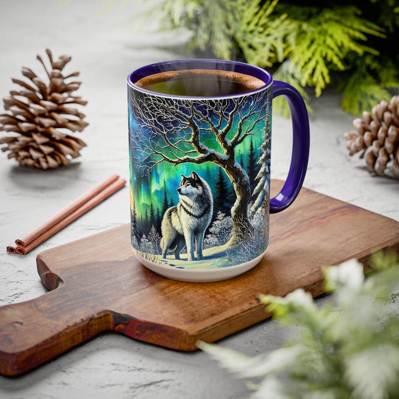 Peut inclure: Mug en c&eacute;ramique blanche avec une anse et un bord violets, orn&eacute; d'une illustration d&eacute;taill&eacute;e d'un loup dans une for&ecirc;t enneig&eacute;e sous une aurore bor&eacute;ale. La tasse est remplie d'un liquide fonc&eacute;.