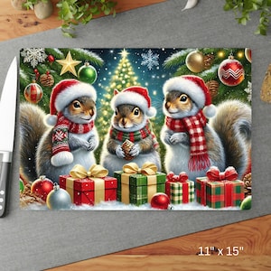 May include: A rectangular cutting board featuring three squirrels wearing Santa hats and scarves, surrounded by Christmas gifts and ornaments. The board measures 11 inches by 15 inches.