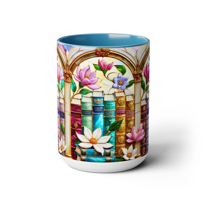 May include: A white ceramic mug with a blue interior. The mug features a colorful stained-glass design of books, flowers, and an archway. Pink, white, and blue flowers are scattered around the books. The mug is a standard size for coffee or tea.