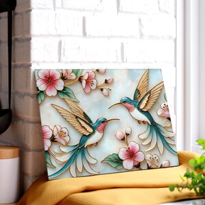 Pode incluir: Pe&ccedil;a de arte retangular decorativa com dois beija-flores com detalhes em azul-petr&oacute;leo, rosa e dourado, rodeados por flores rosa e folhas verdes. A obra de arte tem uma apar&ecirc;ncia texturizada e tridimensional, sobre um fundo azul claro.