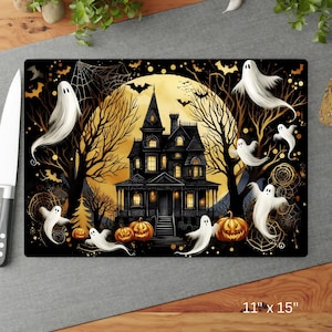 May include: A rectangular Halloween-themed chopping board featuring a spooky haunted house, ghosts, and pumpkins. The design includes a full moon, bats, and spiderwebs. The board measures 28 cm by 38 cm.