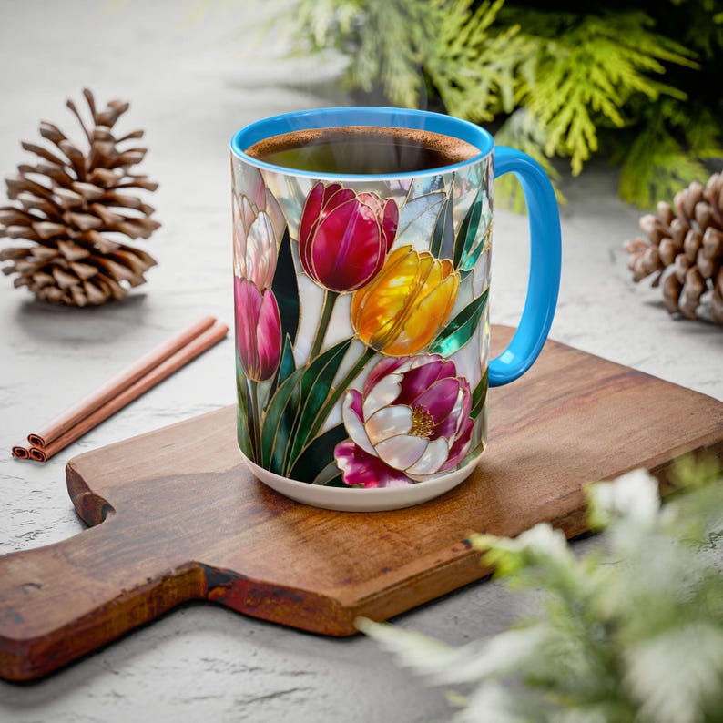 Pu&ograve; includere: Una tazza da caff&egrave; in ceramica con manico e bordo blu, riempita di liquido scuro. La tazza &egrave; decorata con un motivo floreale in stile vetrata con tulipani rossi, gialli e viola. La tazza &egrave; appoggiata su un tagliere di legno.