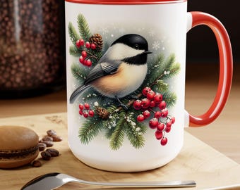 May include: White ceramic mug with a red interior and handle. The mug features a detailed illustration of a chickadee bird perched on a pine branch with red berries and snowflakes. The mug is on a wooden surface.