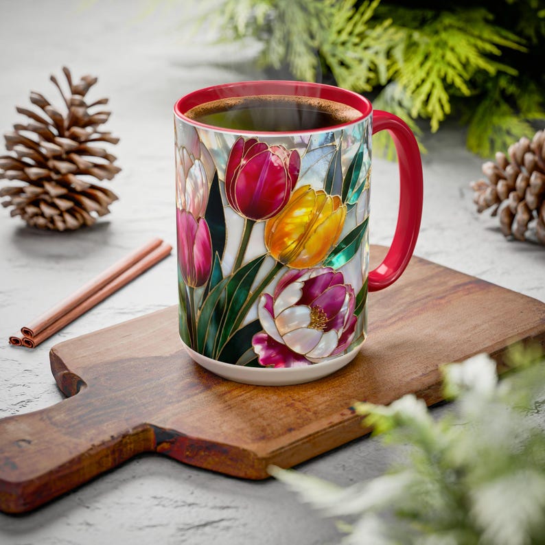Pu&ograve; includere: Una tazza da caff&egrave; in ceramica con manico e bordo rossi, piena di caff&egrave;. La tazza presenta un colorato motivo floreale di tulipani nei toni del rosso, giallo e viola, con foglie verdi. La tazza &egrave; appoggiata su un tagliere di legno.