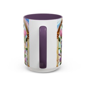 May include: White ceramic mug with a purple interior and handle. The mug features a stained-glass design with pink and purple flowers, gold trim, and a blue sky background. The handle is a solid purple color.