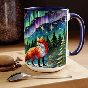May include: White ceramic mug with a vibrant stained-glass design featuring a red fox in a forest under the Northern Lights. The mug has a navy blue handle and interior, and is suitable for hot or cold beverages.