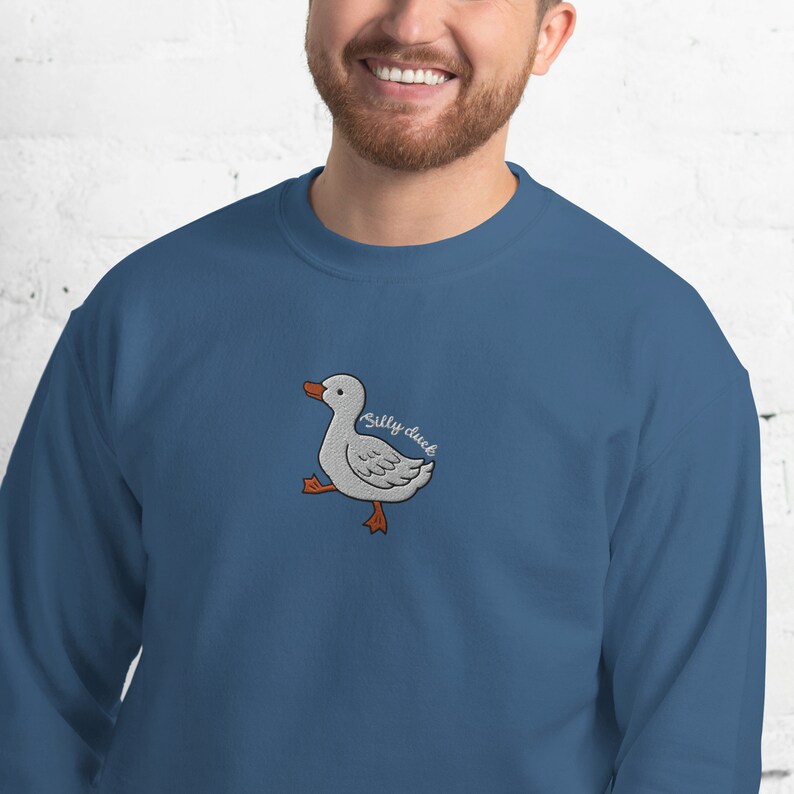May include: A blue sweatshirt with a white embroidered duck and the text "Silly duck" in brown.