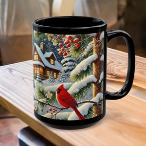 May include: Black ceramic mug featuring a winter scene with a red cardinal perched on a snow-covered branch. The design includes a cozy cabin, pine trees, and red berries, creating a festive holiday theme. The mug has a large handle for easy gripping.