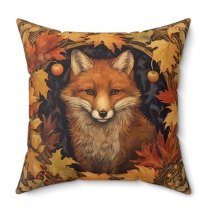 May include: A square throw pillow with a red fox face surrounded by autumn leaves in shades of orange, yellow, and brown. The fox has a white muzzle and a black nose.