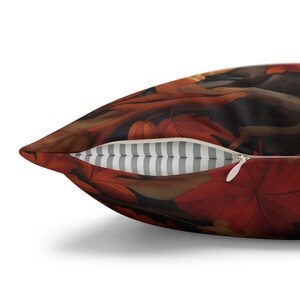 May include: A throw pillow with a zipper closure, featuring a colorful autumn leaf pattern in shades of red, orange, and brown. The pillow has a white and gray striped lining.