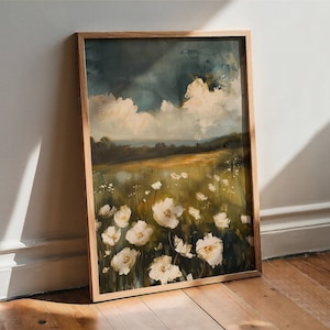 May include: A framed painting of a field of white flowers with a cloudy sky in the background. The painting is in a wooden frame and is leaning against a white wall.