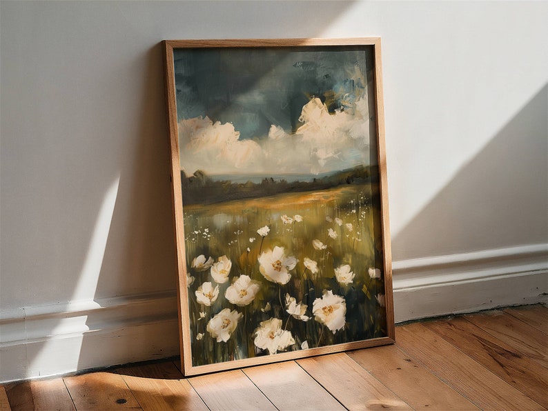May include: A framed painting of a field of white flowers with a cloudy sky in the background. The painting is in a wooden frame and is leaning against a white wall.