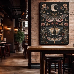 May include: A black canvas print with a dark background featuring three detailed illustrations of moths with intricate wings and a crescent moon with stars. The moths are surrounded by floral elements in shades of pink, red, and white.
